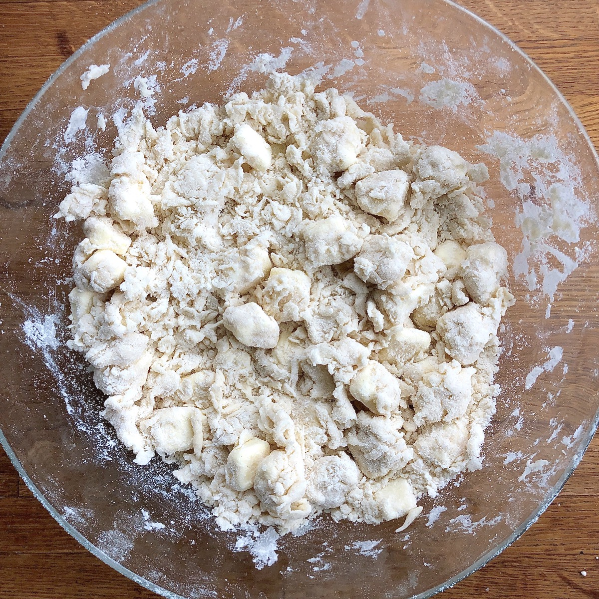 Clumps of pie dough in a bowl, dry but starting to become cohesive.