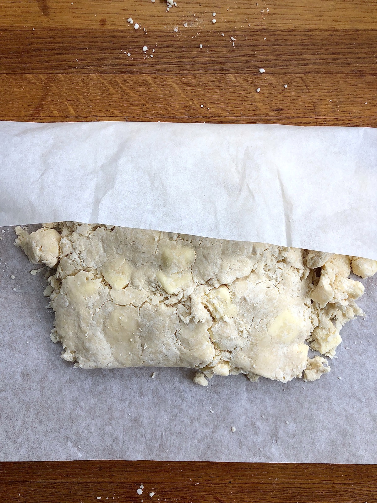 Clumps of pie dough pressed atop one another with the aid of parchment paper