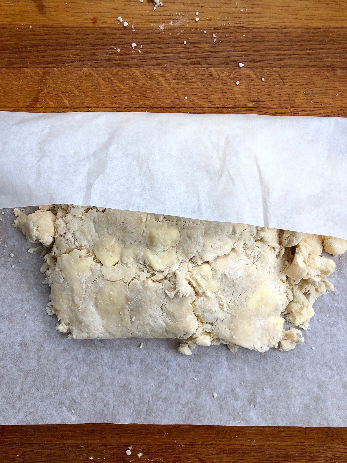 Clumps of pie dough pressed atop one another with the aid of parchment paper