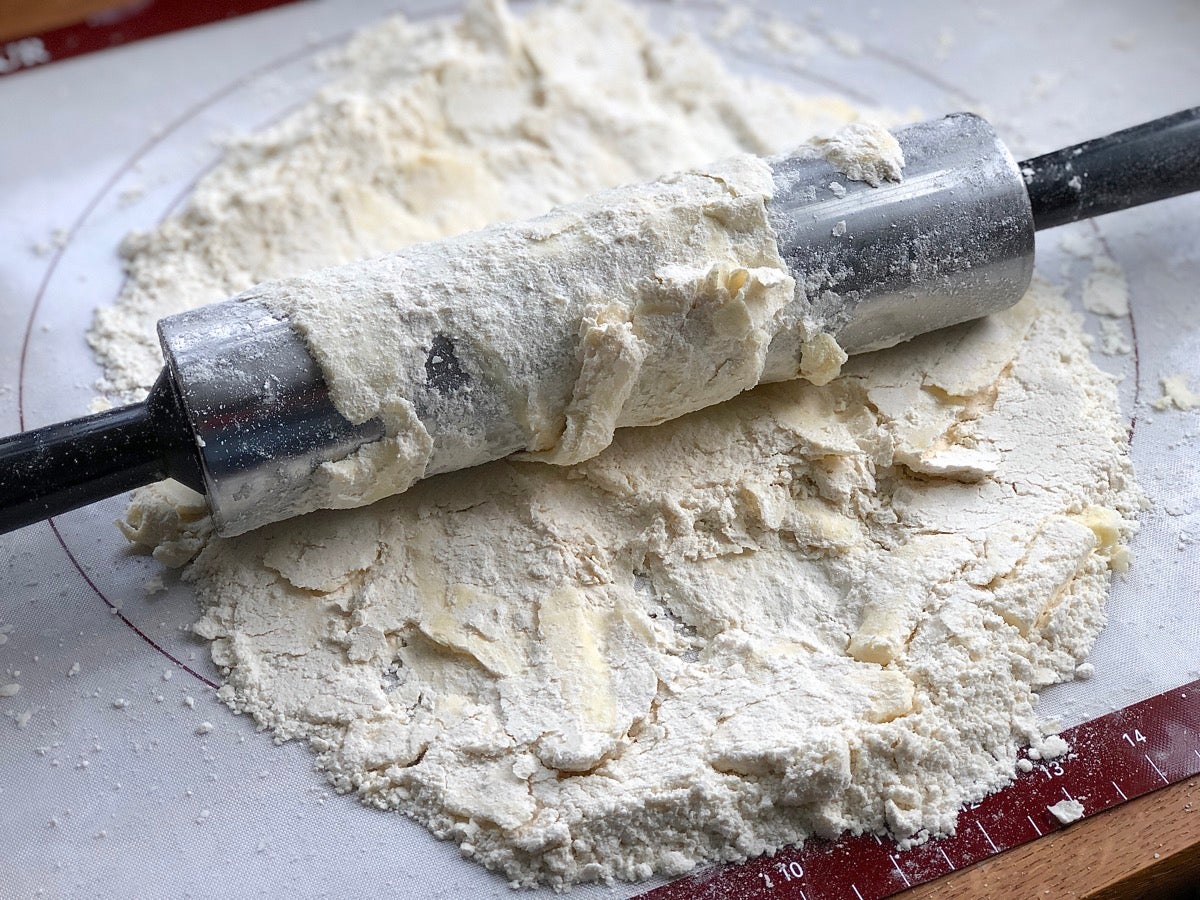 Strips of cold butter tossed with flour and being rolled flat on a silicone mat.