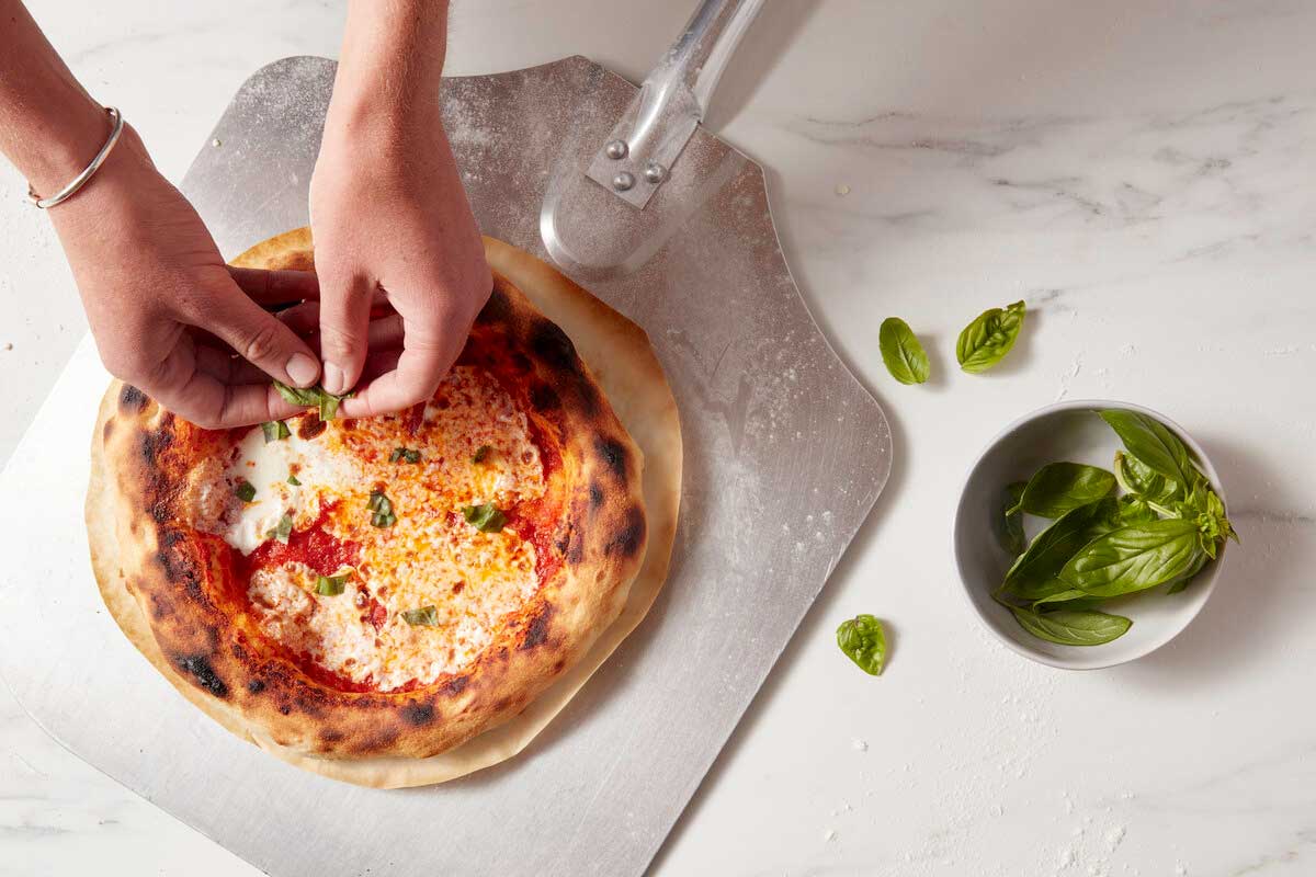 Baked pizza being garnished with basil