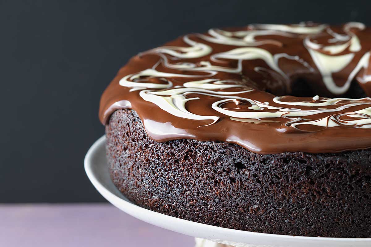 A vegan chocolate cake covered with chocolate ganache on a cake stand
