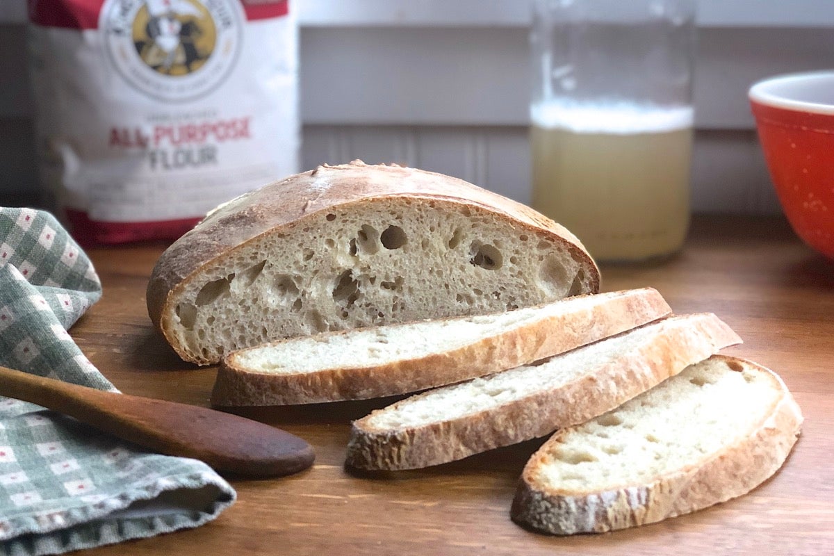 Loaf of sliced bread on a table with a bottle of yeast water and bag of flour.