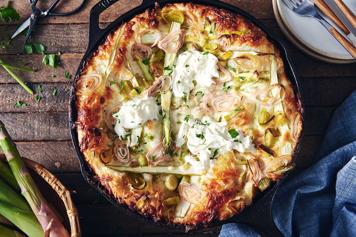 Crispy Cheesy Pan Pizza in a cast iron pan topped with asparaus, leeks, shallots, and burratta