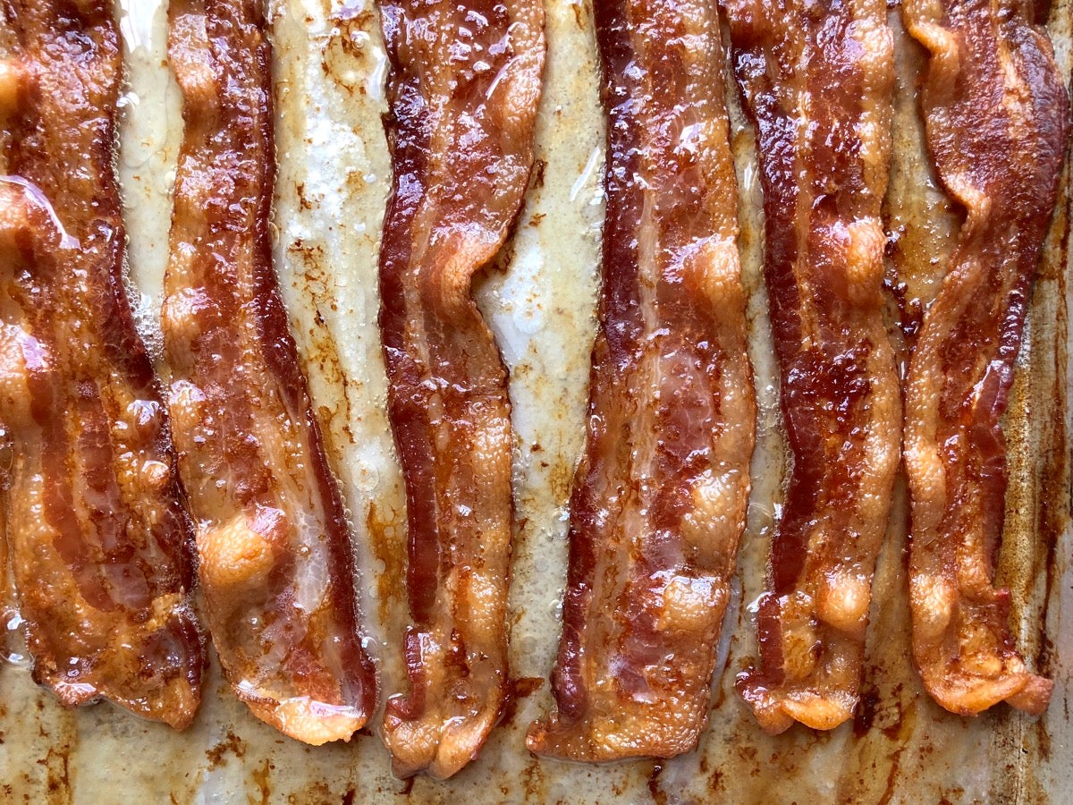 Baked bacon sizzling on a parchment-lined baking sheet.