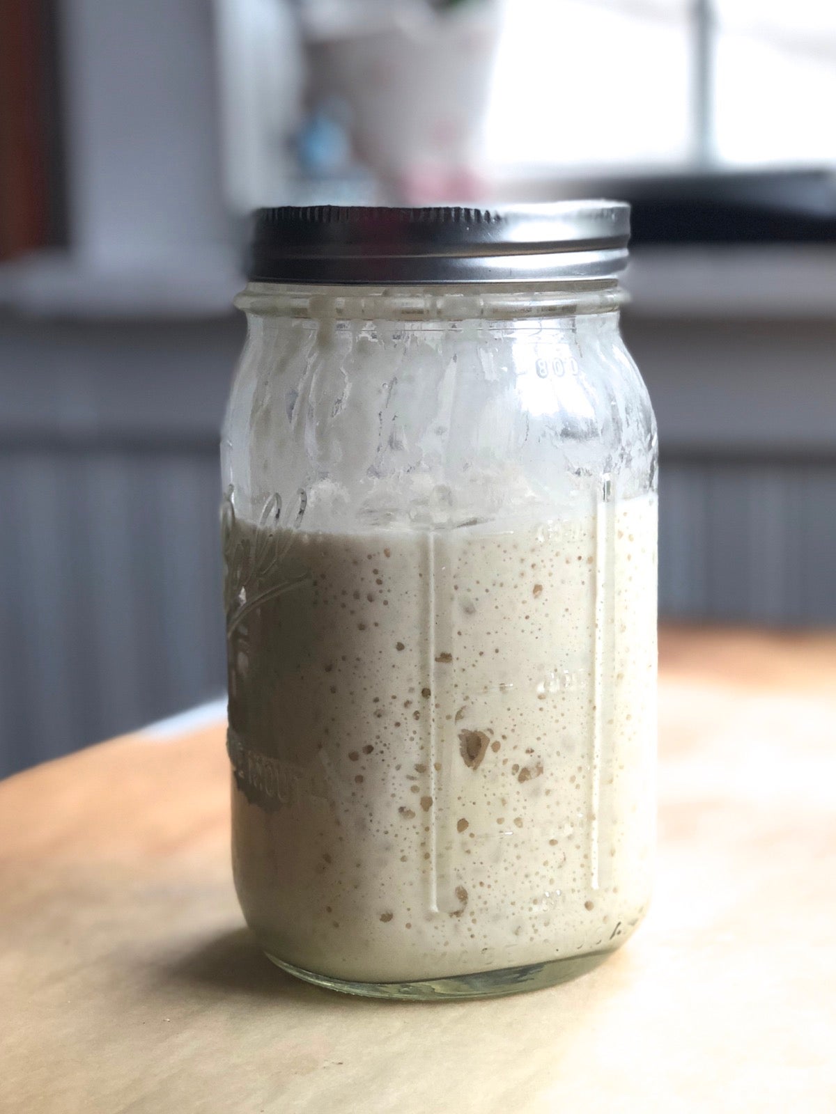 Sourdough starter bubbling in a jar on a table.