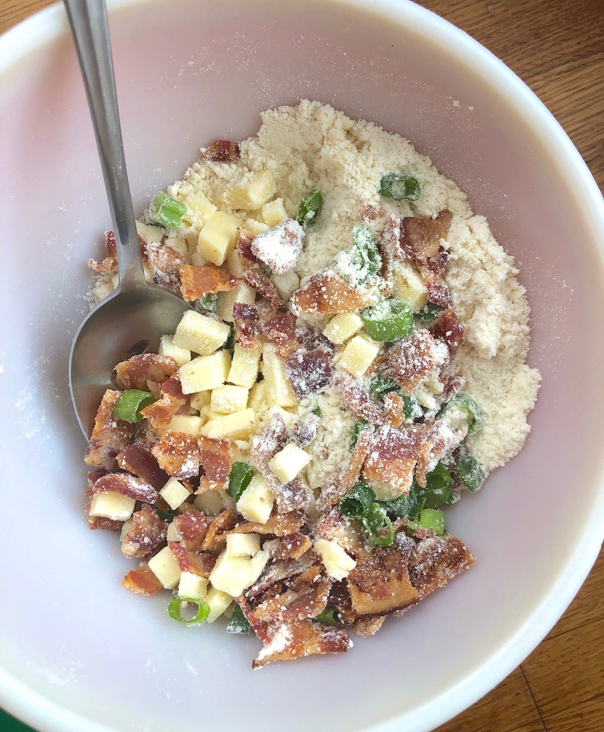 Dry ingredients, cooked, crumbled bacon, subes of cheddar cheese and snipped scallion greens stirred together in a bowl.