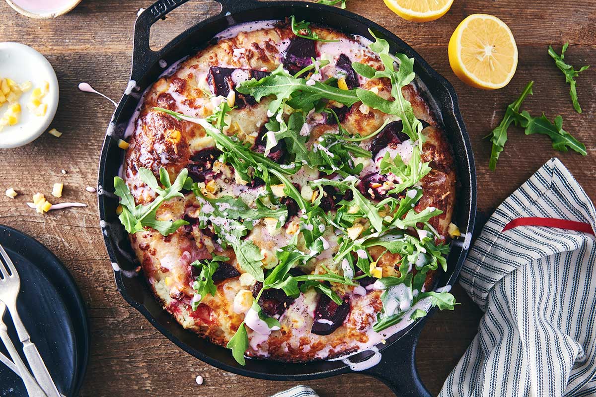 Crispy Cheesy Pan Pizza in a cast iron pan topped with beet, feta, meyer lemon, and arugula