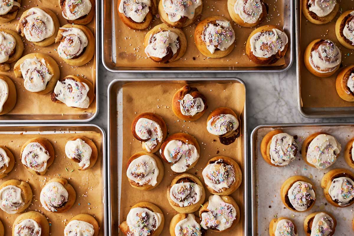 Baked cinnamon rolls on sheet pans with icing and sprinkles