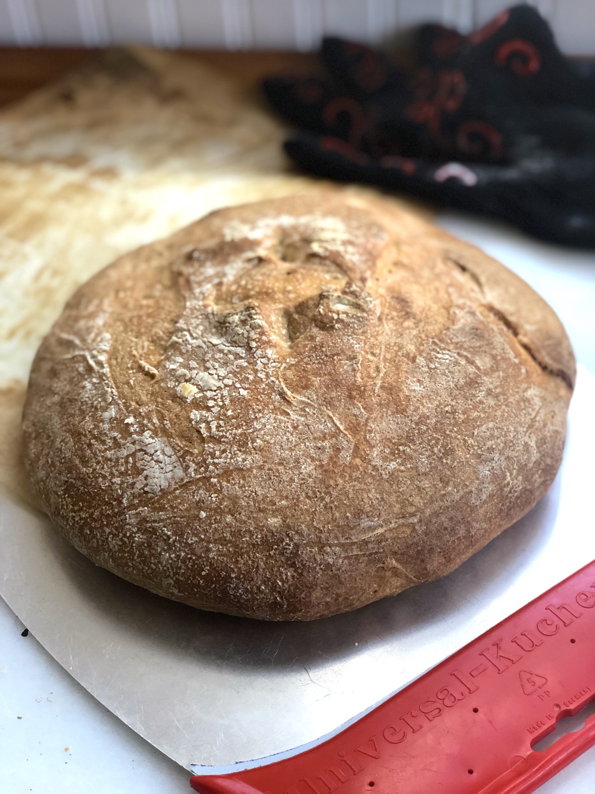 Round, flat loaf of sourdough bread, just out of the oven on a peel.