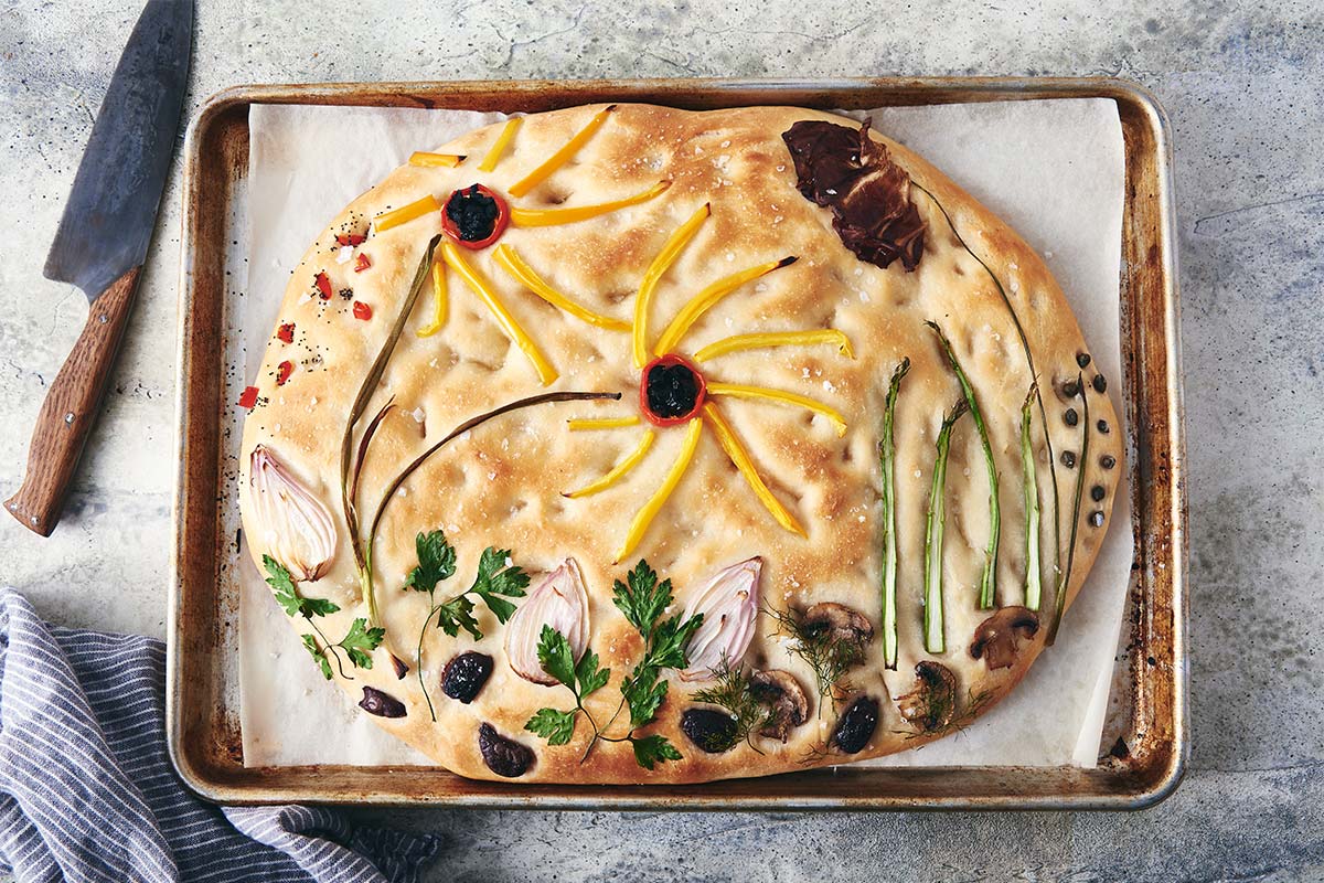 A baked garden focaccia, topped with vegetables artfully arranged like flowers