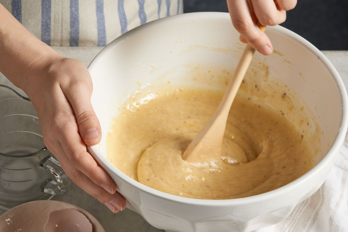 Hands mixing cake batter with wooden spoon