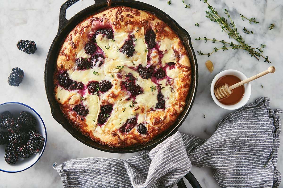 A cast iron pan pizza topped with honey, ricotta, blackberries, and brie