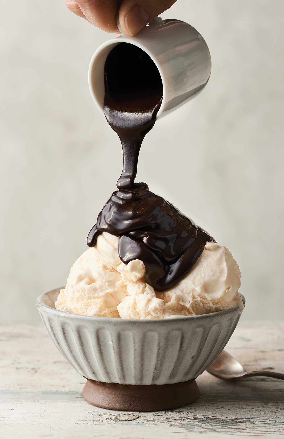 A bowl of vanilla ice cream that's being topped with hot fudge sauce