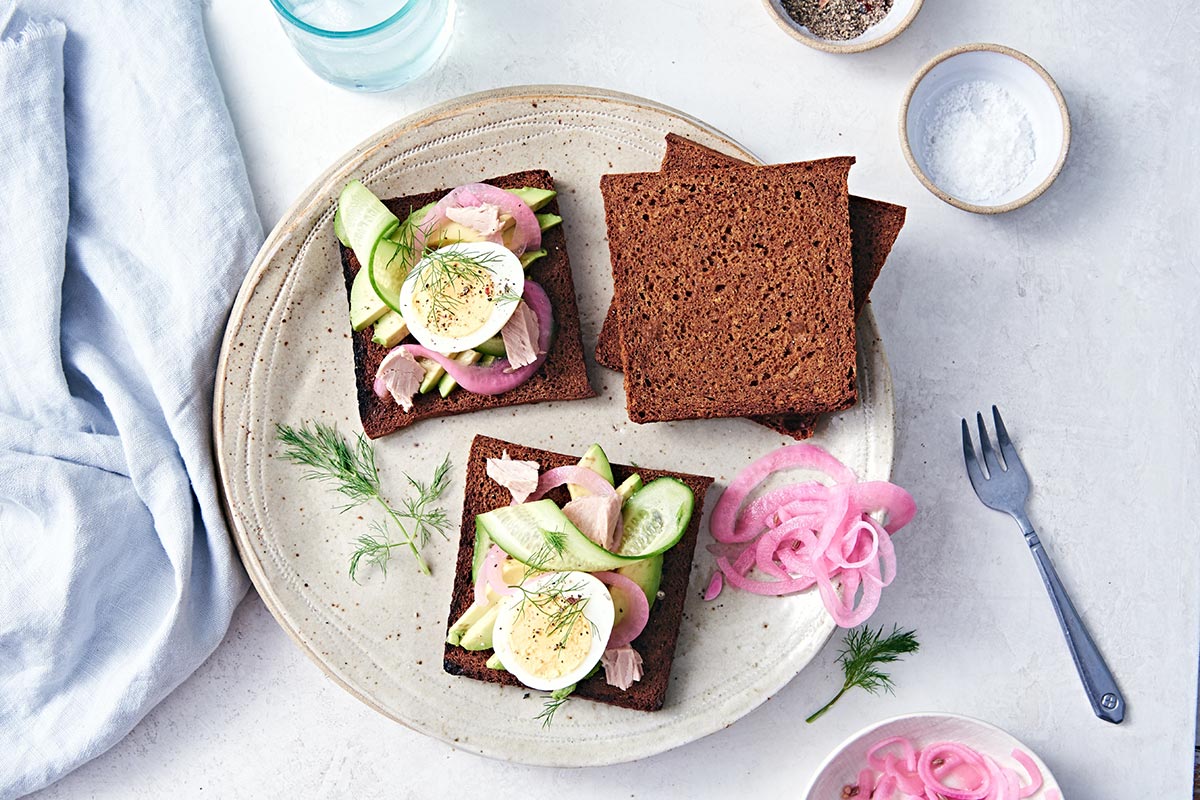 A loaf of icelandic rye bread cut into thin slices and topped with smoked fish