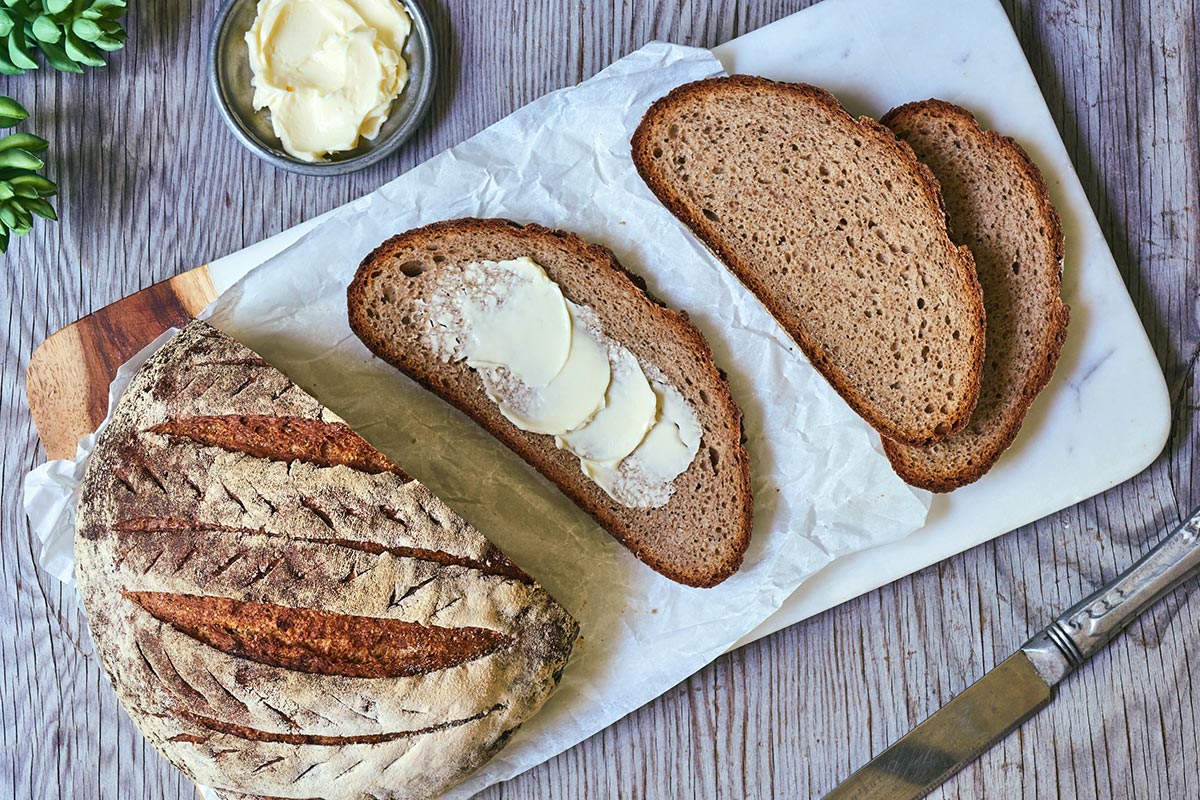 A loaf of sourdough rye bread with a few slices cut, topped with butter