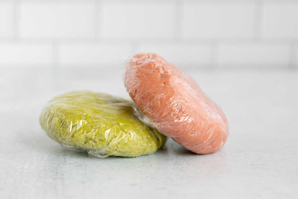 Wrapped discs of green and pink dough on counter