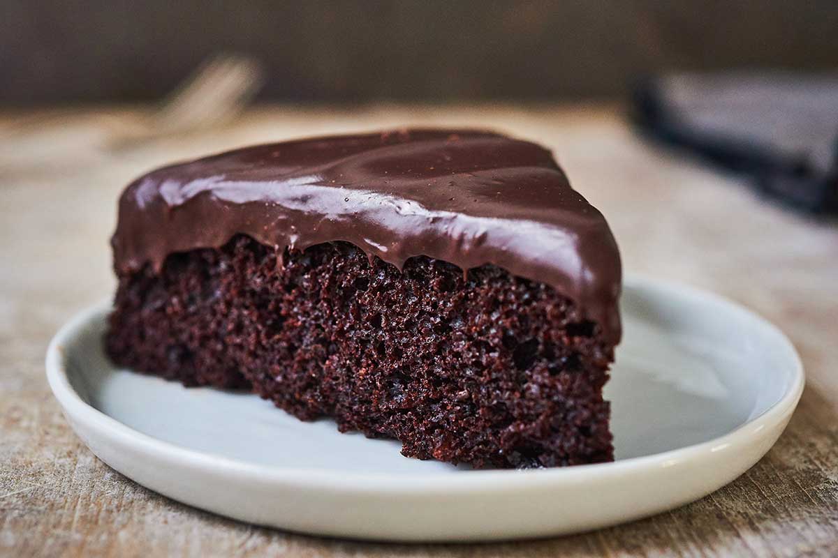 A slice of chocolate cake on a plate topped with chocolate ganache