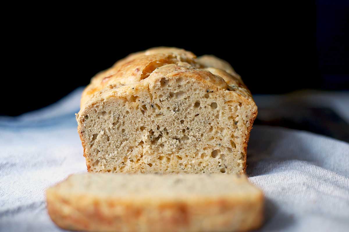 A loaf of cheddar cheese rosemary bread sliced on a cutting board