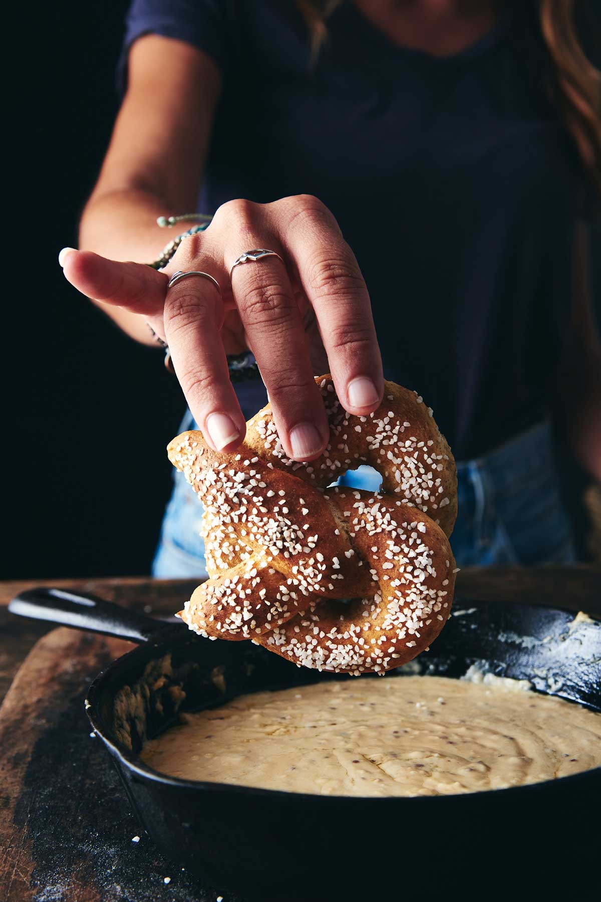 Baker dipping rye pretzel into cheese sauce