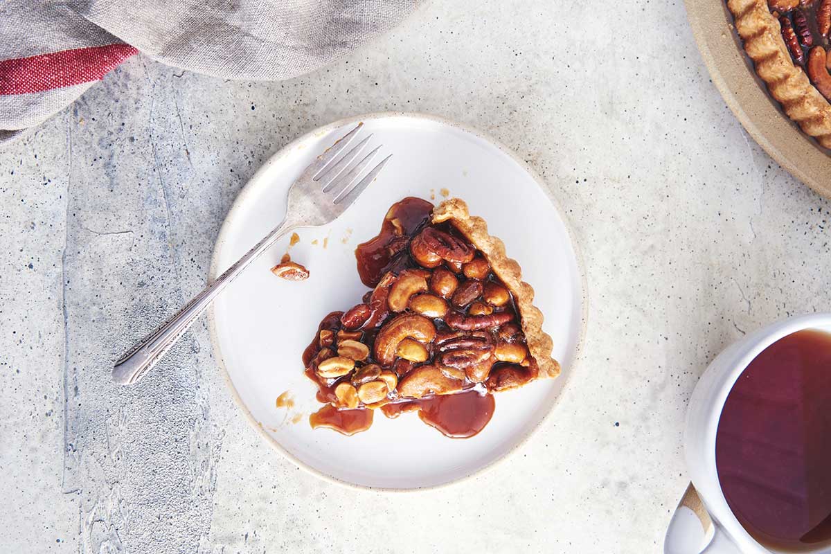 Slice of salted caramel nut tart with rye crust on a plate