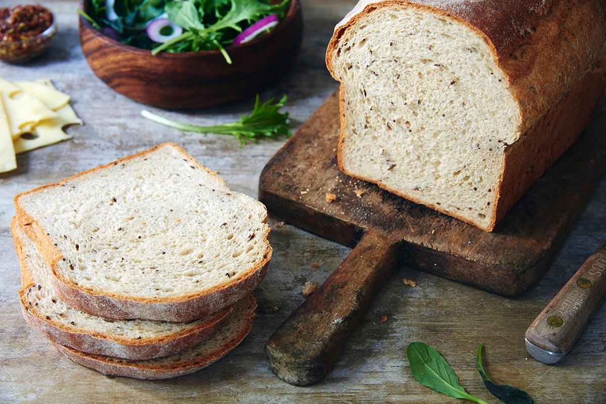 A loaf of seeded rye sandwich bread with a few slices cut