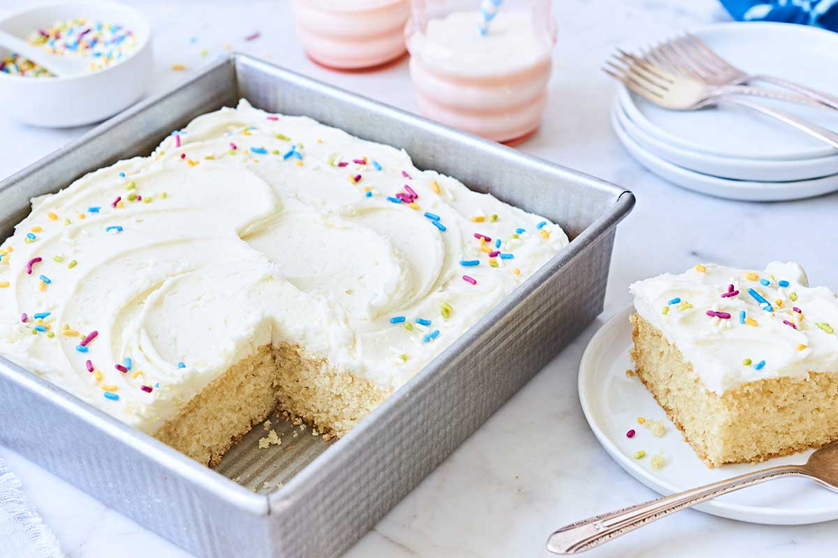 A vanilla cake pan cake with a slice removed, topped with colorful sprinkles