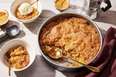 A round pan of Sugar-Crusted Apple Cobbler with a spoonful portioned into a small bowl.
