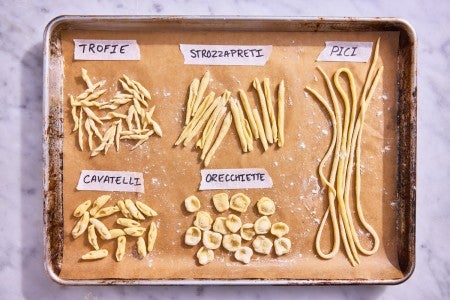 Different hand-shaped pasta types on a parchment-lined baking sheet