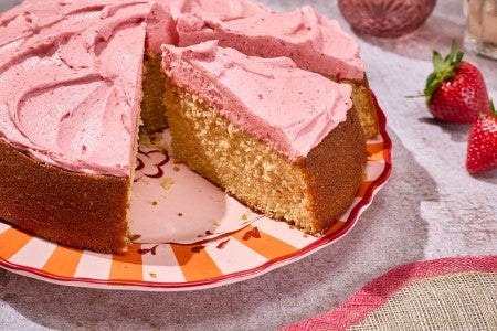 Brown Sugar Strawberry Frosted Cake seen from the side showing a thick layer of frosting and a golden cakey interior.