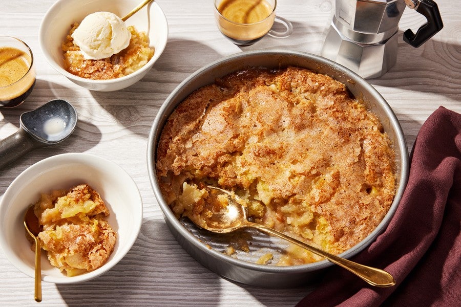 A round pan of Sugar-Crusted Apple Cobbler with a spoonful portioned into a small bowl.