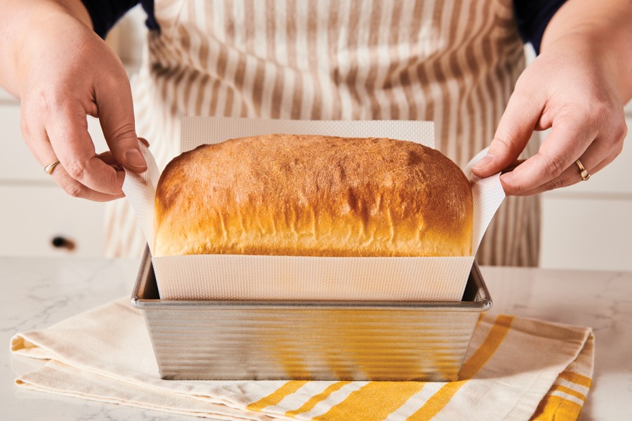 Baker lifting loaf of bread out of pan with silicone pan liner