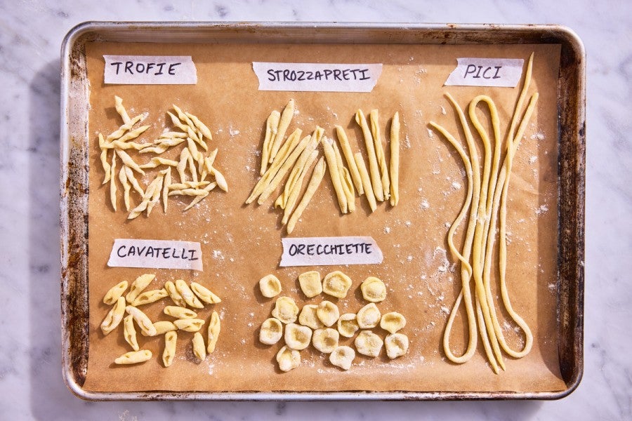 Different hand-shaped pasta types on a parchment-lined baking sheet