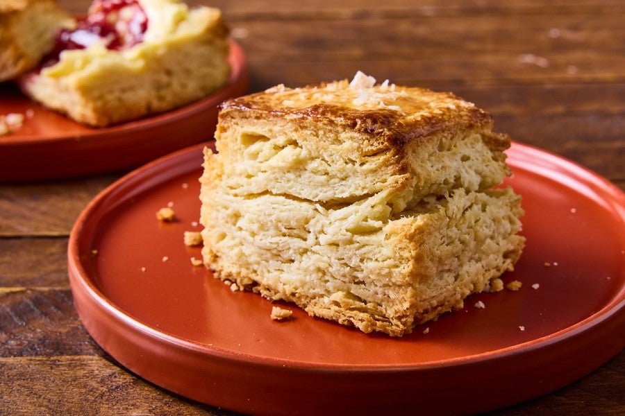 Side view of a tall ultimate flaky biscuit that clearly shows horizontal layers in the biscuit, a perfect golden baked exterior, and a bit of salt on top.