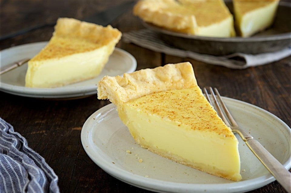 Two slices of custard pie on plates with the rest of the pie in the background