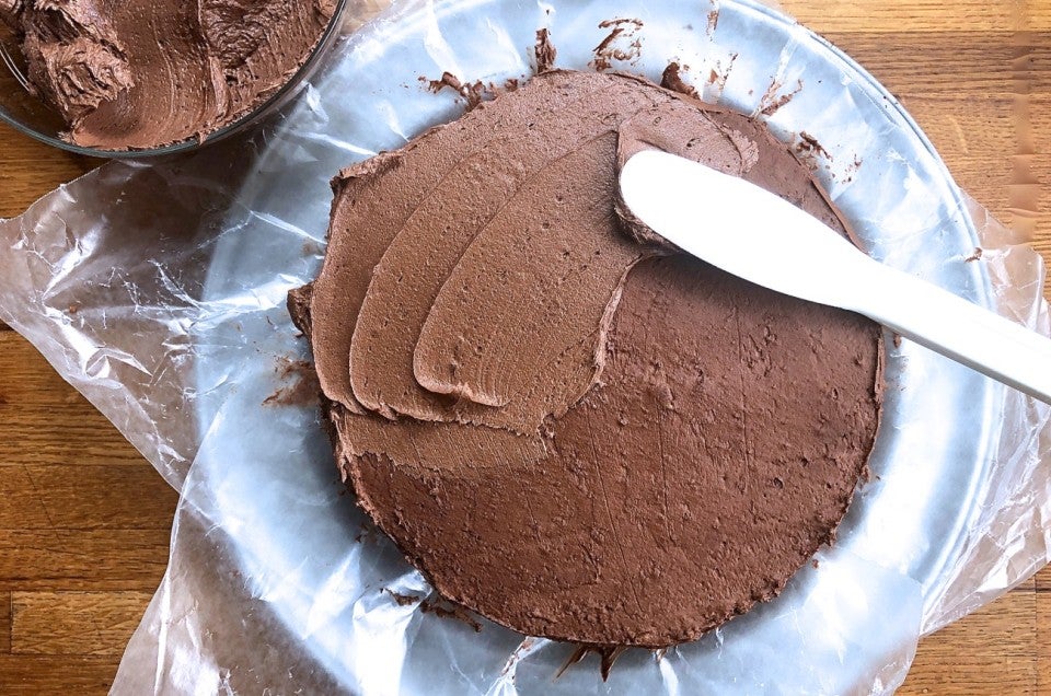 Yellow layer cake with a chocolate crumb coat, final layer of icing being applied on top.