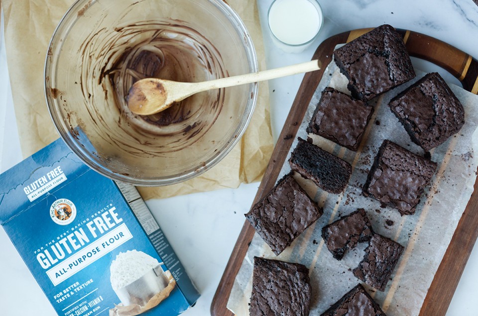 Gluten-free brownies with a box of gluten-free flour, a mixing bowl, and a glass of milk