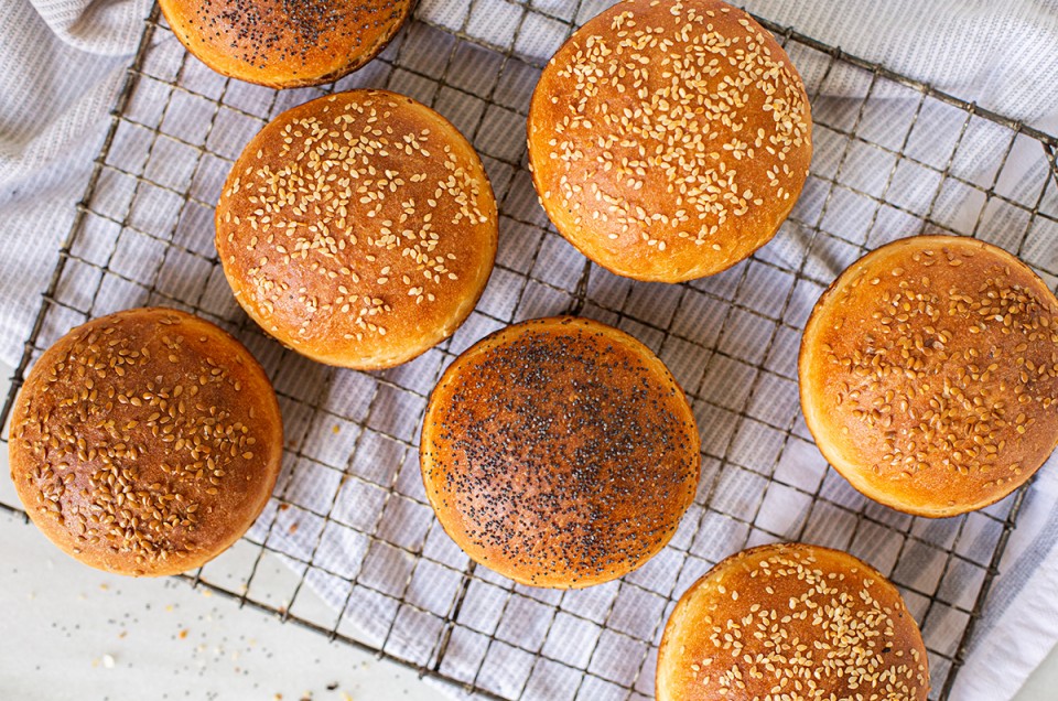 Homemade hamburger buns topped with seeds cooling on a rack