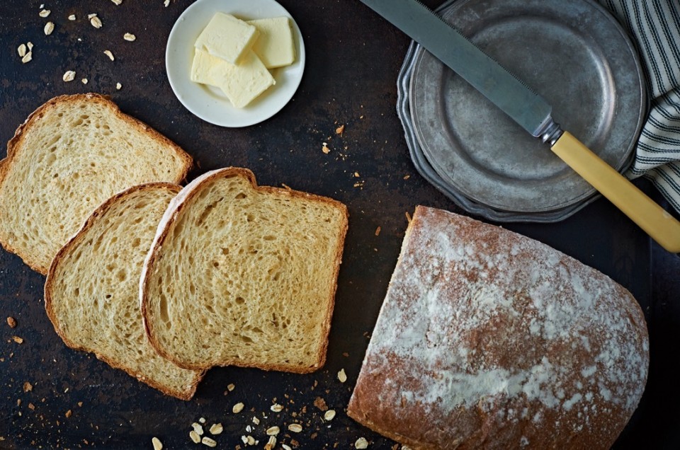 Loaf of oatmeal bread sliced, with knife and saucer of butter pats