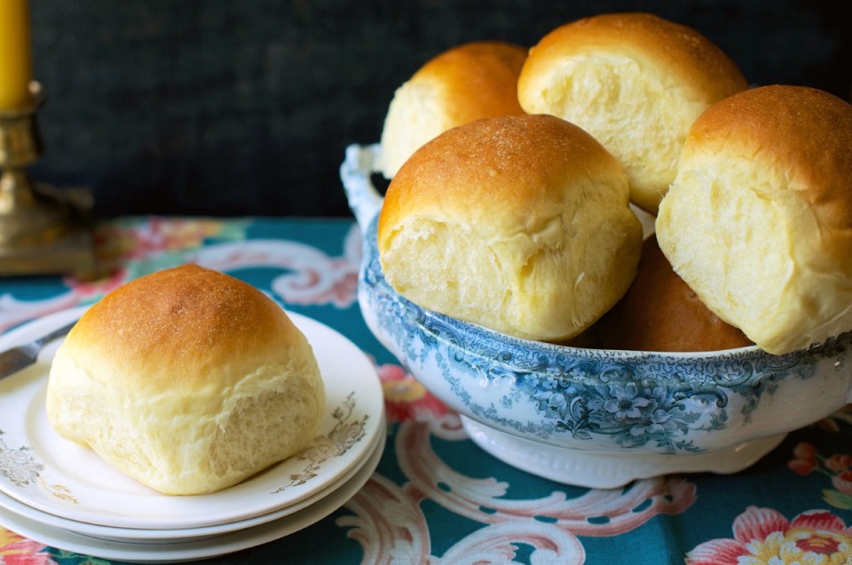 Golden soft dinner rolls in a bowl, one on a bread plate.
