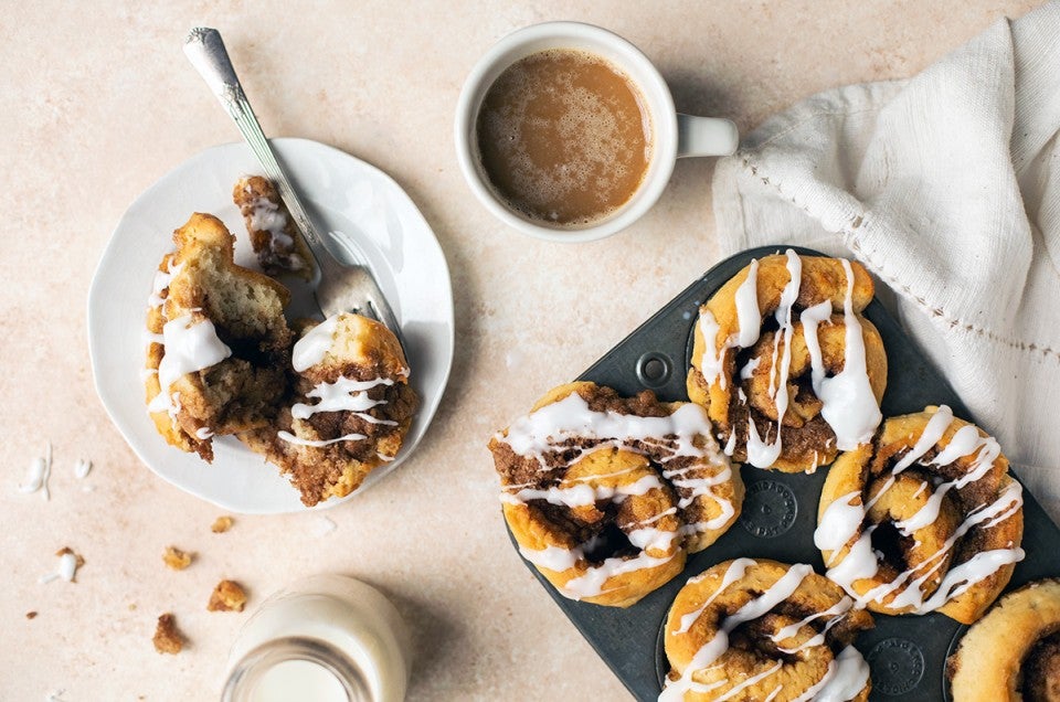 A tray of gluten-free cinnamon rolls next to a cup of coffee and plate with a cinnamon roll on it