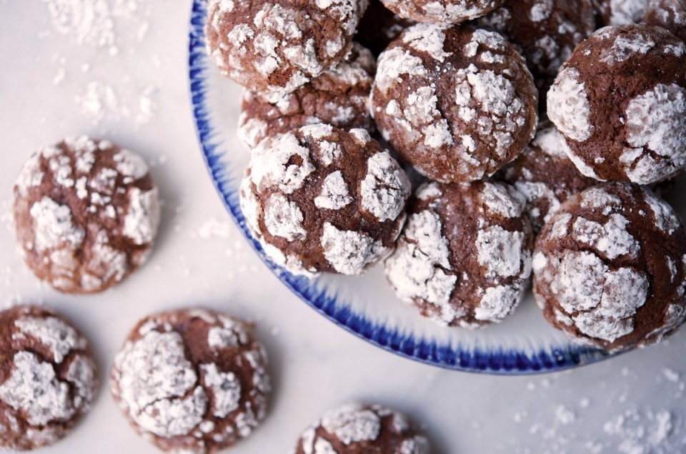 A platter of chocolate crinkles next to a few scattered cookies on a table