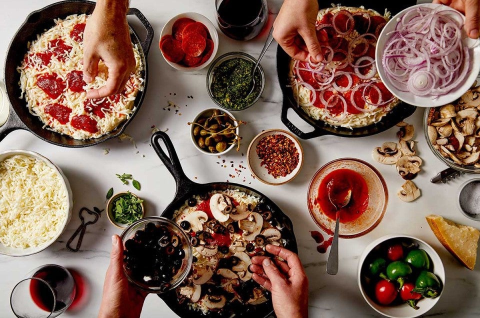 Three cast iron pan pizzas being topped with different ingredients