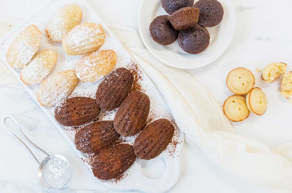 A platter of chocolate and vanilla madeleines shaped traditionally next to a few madelelines shaped like mini muffins