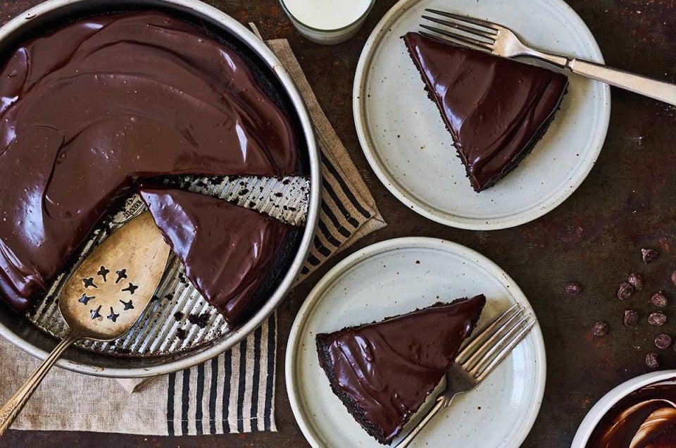 A chocolate cake pan cake topped with chocolate frosting and a few slices on plates