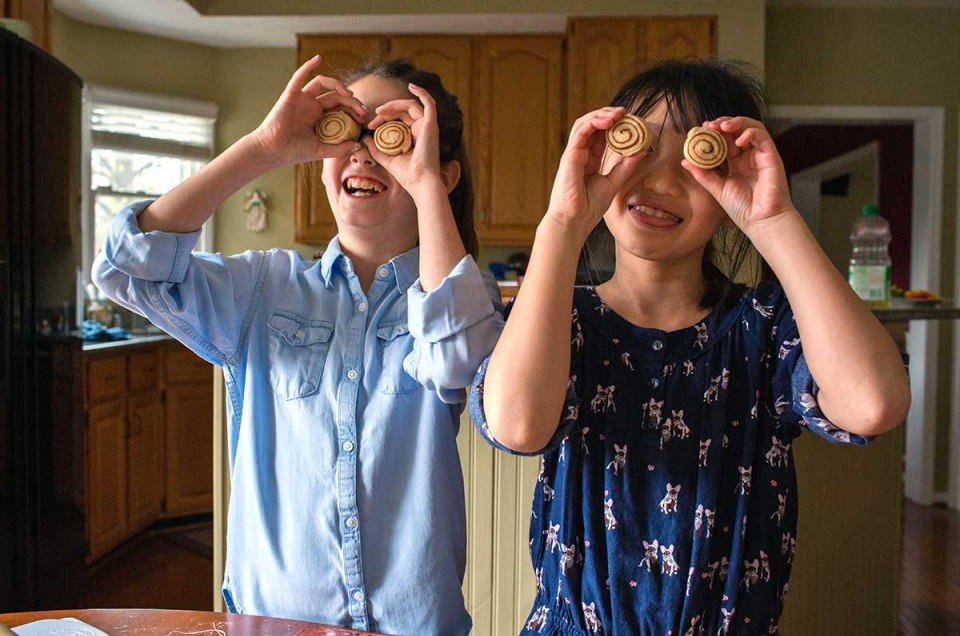 Two older kids being silly by holding cinnamon rolls up as if they were eyes