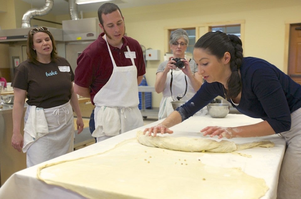 Woman rolling pastry on large table.