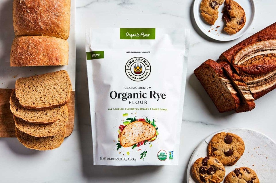 A loaf of rye sandwich bread, rye banana bread, and rye chocolate chip cookies next to a bag of rye flour