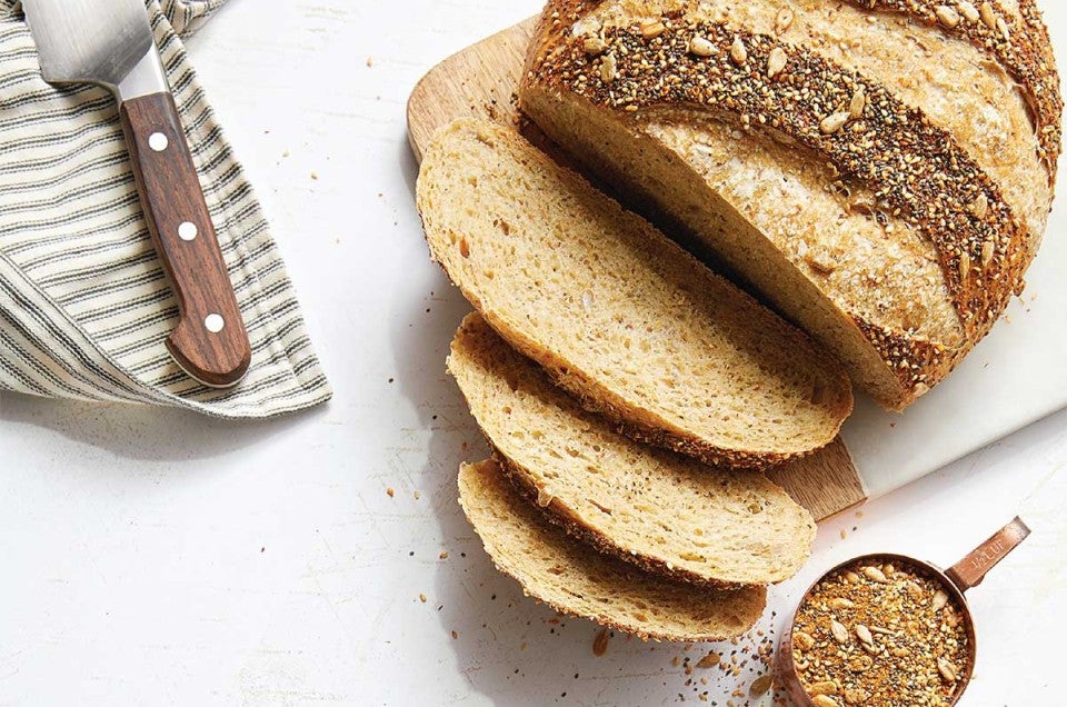 Sliced seeded sourdough next to cup of grains