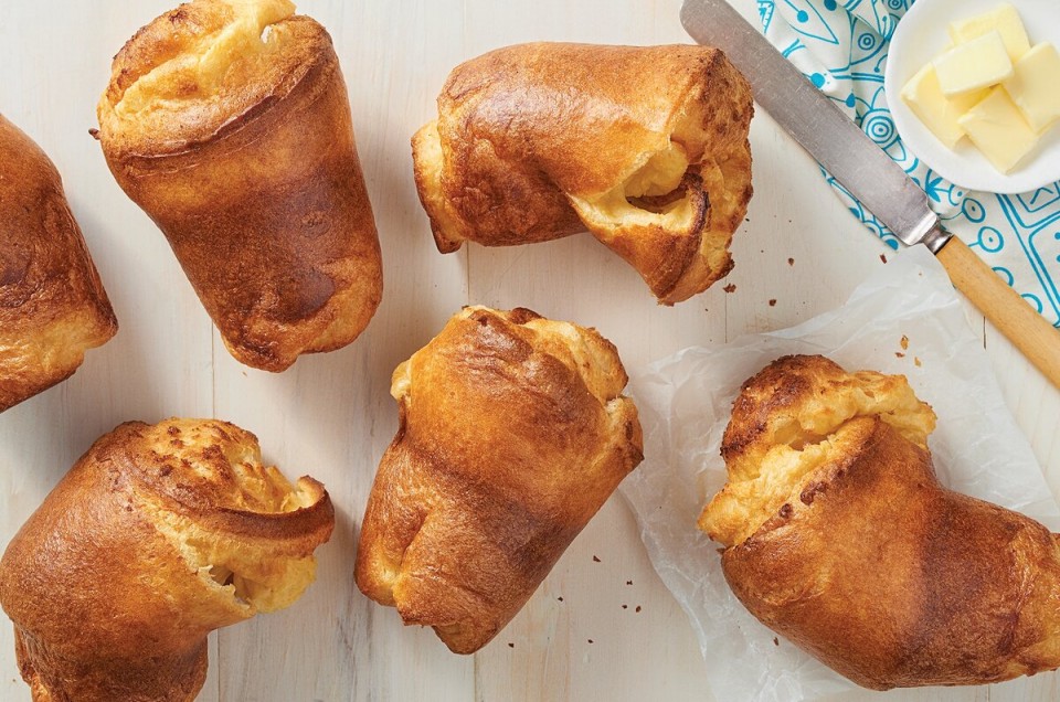 A set of six baked popovers next to a ramekin of butter